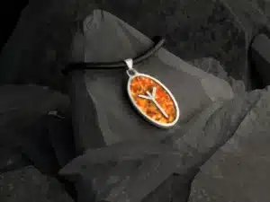 Vedhæng i sølv med Algiz-rune og rav, placeret på mørk stenbaggrund. Vikingesmykke med nordisk symbolik og håndlavet design.